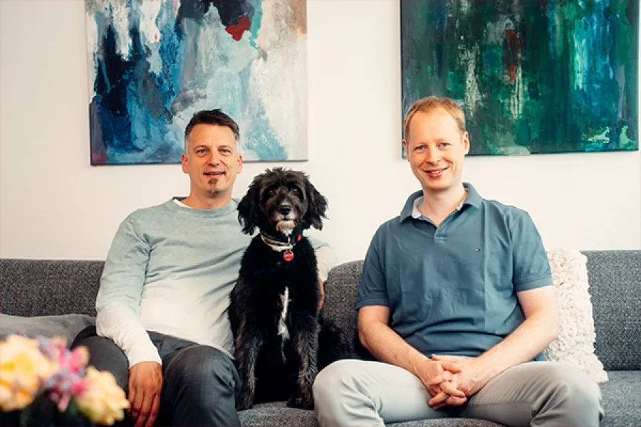 Zwei Kollegen aus dem rose-Team mit einem Hund auf dem Sofa